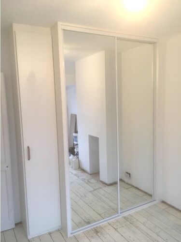 Mirror sliding door wardrobes with adjoining hinged door cupboard with shelves.