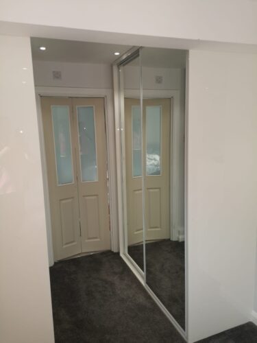 Sliding Wardrobes By En Suite. Mirror doors robes in white profile on both sides of the corridor.