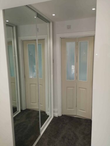 Sliding Wardrobes By En Suite. Mirror doors robes in white profile on both sides of the corridor.